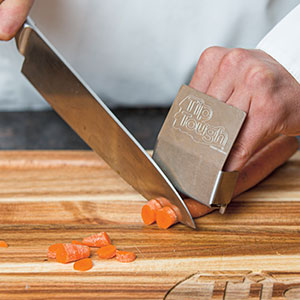 Person cutting carrots with knife while using a metal protection device for their fingers