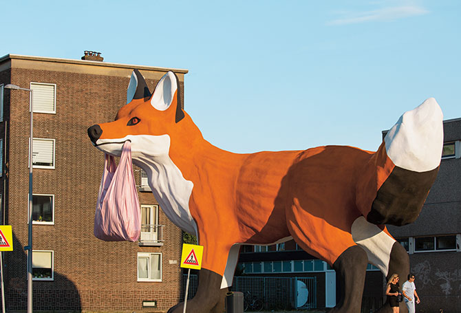 A statue of a fox as tall as an apartment building, holding a plastic bag in its mouth